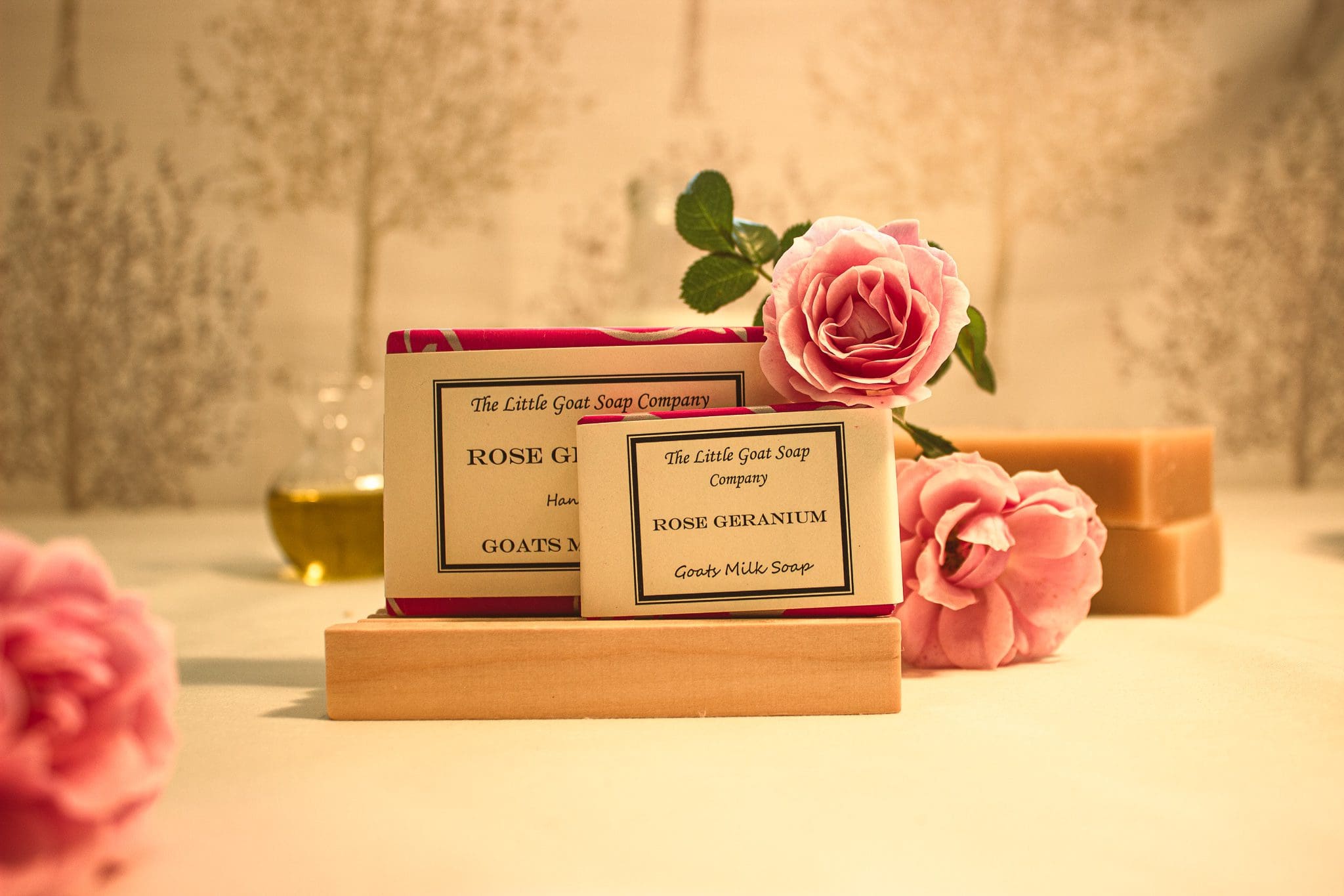 Rose Geranium soap from The Little Goat Soap Company set dressed with pink roses and bars of unwrapped soap