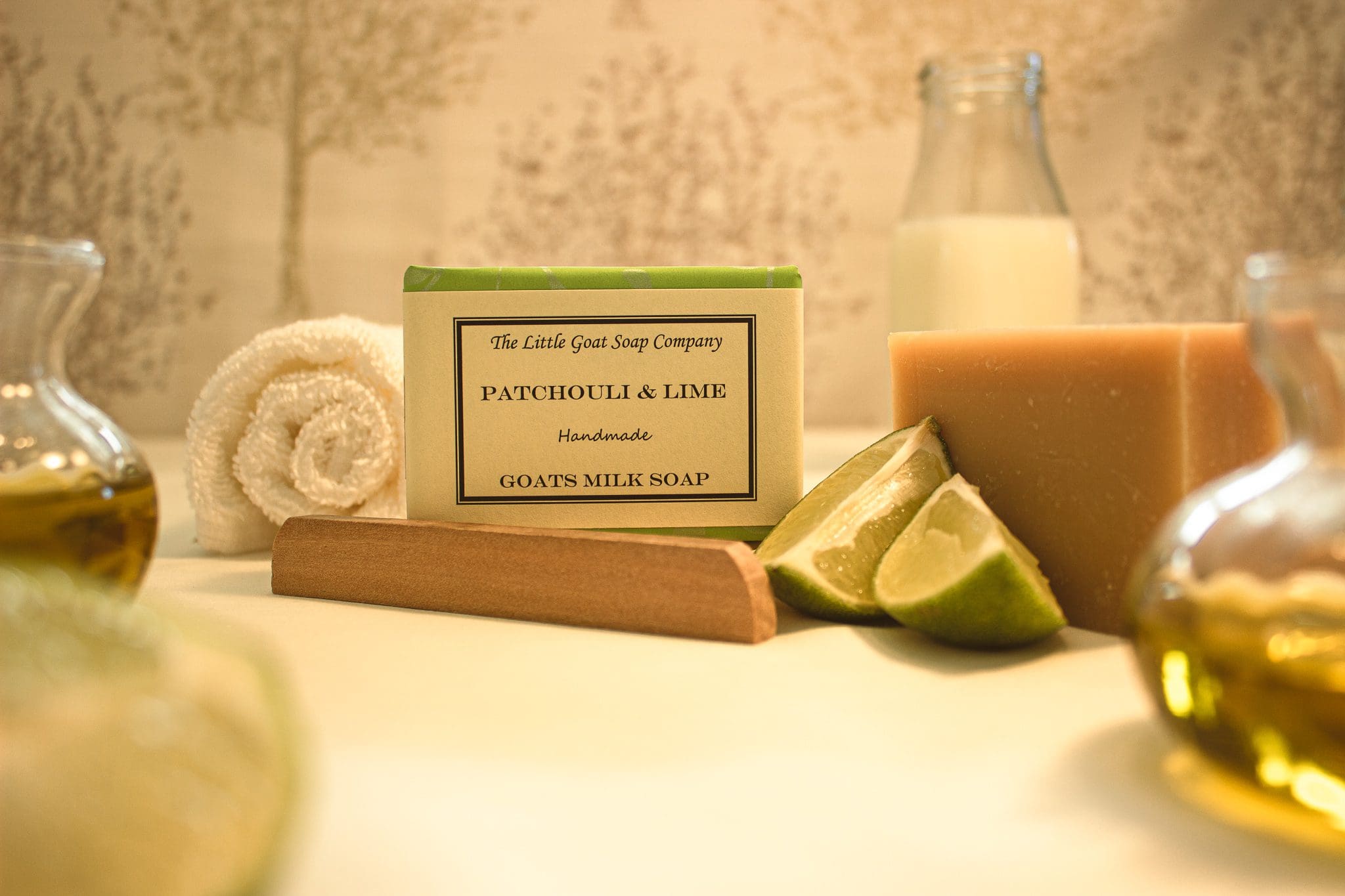 patchouli and lime soap from the little goat soap company set dressed with a rolled flannel, lime wedges and jars of oil and goat milk