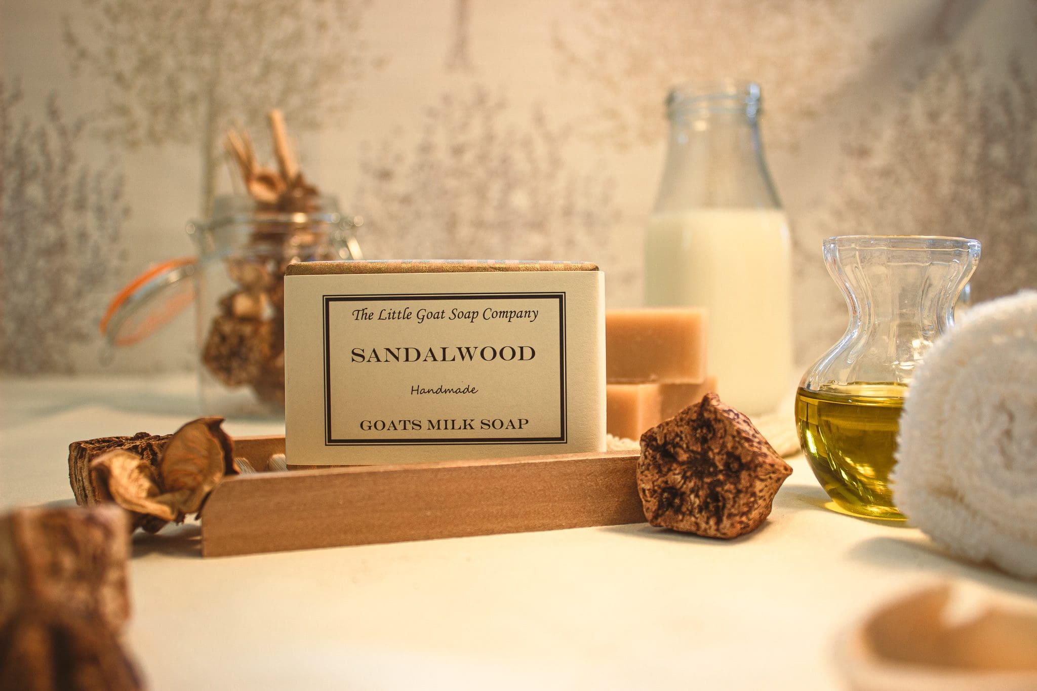 Sandalwood soap from the little goat soap company set dressed with pieces of sandalwood, jars of oil and a bottle of goat milk soap