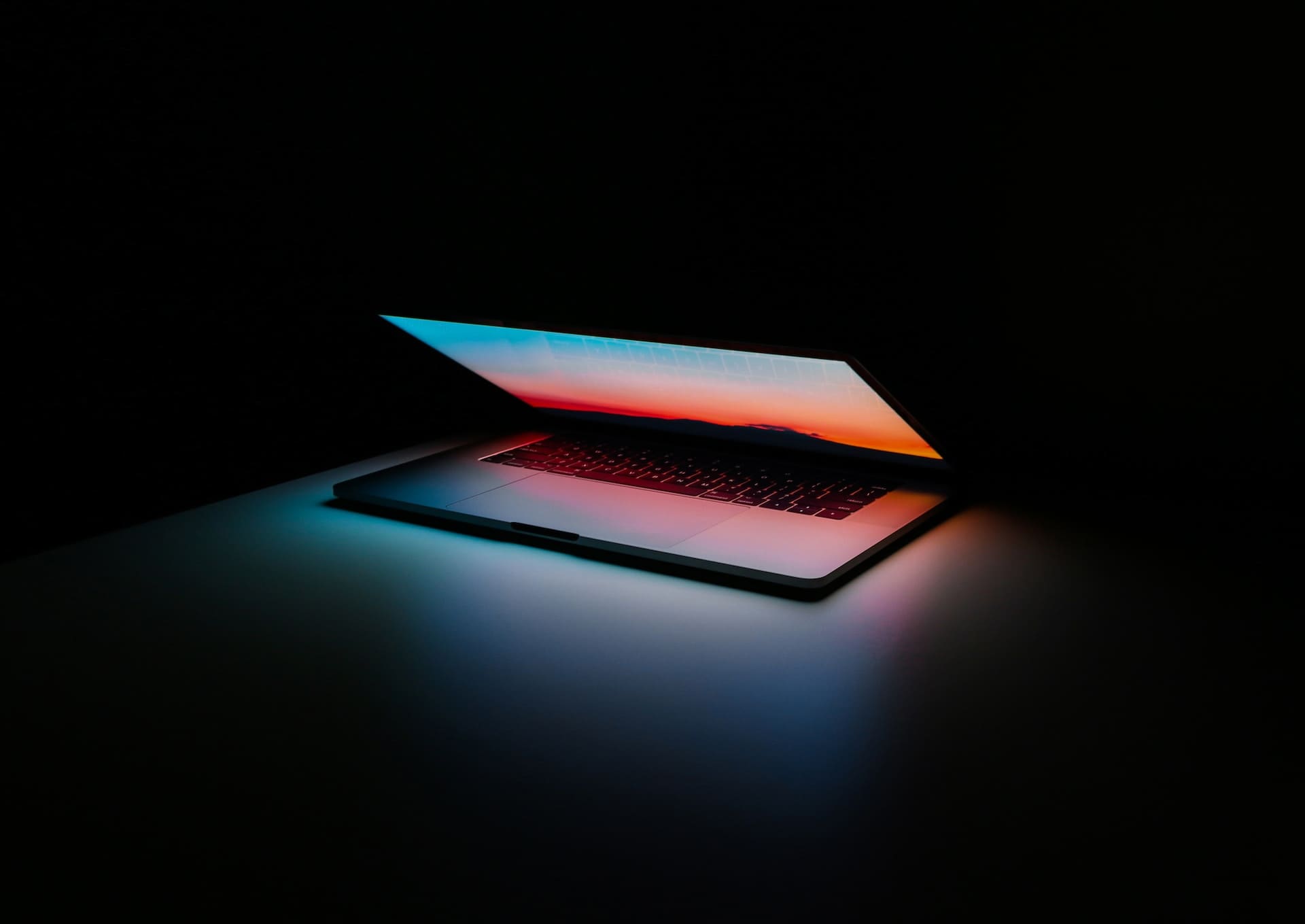 picture of a partially opened laptop in a darkbox studio environment, the laptop screen is illuminating the centre of the screen with blue and orange hues.